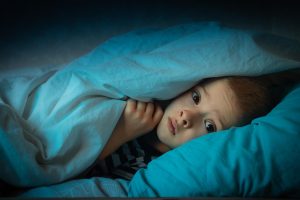 criança escondida embaixo do edredon com medo à noite