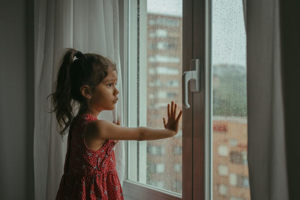 Menina triste olhando pela janela aguardando o pai ausente